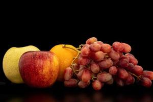 apelsin, vindruvor, äpple och pyrus pyriflora på en svart bakgrund. foto