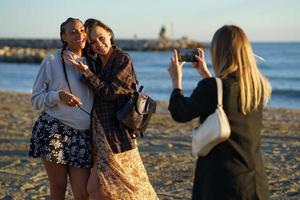 ansiktslös kvinna som fotograferar glada olika flickvänner på stranden foto