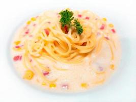 spaghetti pasta carbonara autentisk, traditionell italiensk mat med en mild smak. utsökt recept. toppad med skinka och majsgräddsås, garnerad med bladpersilja och serverad på en vit tallrik. foto