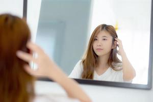 vacker av porträtt asiatisk ung kvinna som undersöker med ansikte och leende tittar på spegeln i sovrummet, flickans skönhet av smink och klädd upp med reflektion, livsstil och wellness-koncept. foto