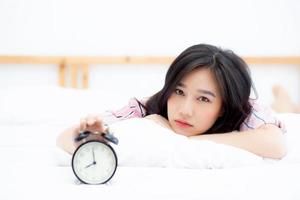 vacker asiatisk ung kvinna stänger av väckarklockan på morgonen, vaknar för att sova med väckarklockan, koppla av och livsstilskoncept. foto