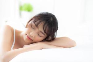 livsstil vackert porträtt ung asiatisk kvinna koppla av liggande sömn och le medan vaknar med soluppgången på morgonen, tjej med glad och rolig i sovrummet, hälsa och välbefinnande koncept. foto