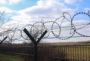 taggtråd mot en molnig himmel på ett stort staket vid en gräns. foto