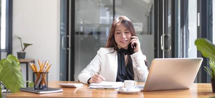 vacker ung asiatisk kvinna sitter på kafé med smartphone. glad ung affärskvinna sitter vid bordet i café med tab top dator. foto