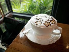 cappuccino med färskt mjölkskum och lattekonst i ett vitt keramiskt glas på ett träbord på ett kafé. foto