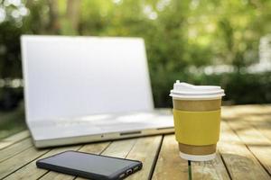 kaffekopp papper med en bärbar dator i grön natur bakgrund. arbeta på distans eller hemifrån. mjukt fokus.effekt för grunt fokus. foto
