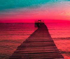 havsutsikt solnedgång med en träpir som sträcker sig ut mot havet och molnig himmel för resor i semestern, slappna av som sommar foto