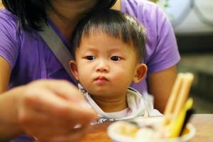 mamma matar mat till sin son under middag på restaurang. asiatisk baby som äter med mamma. foto