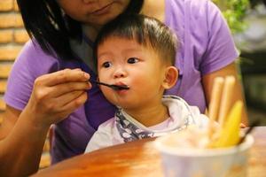 mamma matar mat till sin son under middag på restaurang. asiatisk baby som äter med mamma. foto