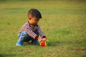 asiatisk pojke spelar fotboll i parken. unge med boll leksak i gräsplan. foto