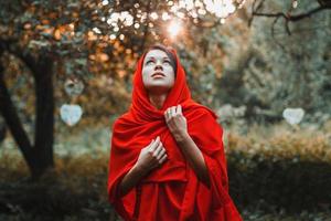 flicka i en röd klänning stående titta upp i trädgården med hjärtan foto