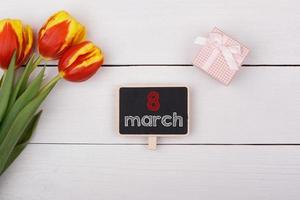 tavla med 8 mars på bordet, bukett tulpaner och en present med en rosett. foto