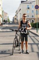 ung hipster man med cykel promenader i staden. svart t-shirt med tryck 23 foto