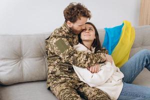 ukrainskt par, militär man i uniform med sin flickvän på soffan hemma på en bakgrund av gul och blå flagg foto
