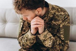 porträtt av känslomässig ung skäggig ukrainsk patriotsoldat i militäruniform sittande på kontorssoffan foto