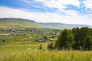 pittoreska landskapet i en liten by bland bergen på sommaren. små hus bland grönt gräs och träd. foto