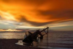 övergivet skeppsvrak av trä fiskebåt på stranden vid skymningstid foto