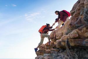 ungt asiatiskt par klättrar upp på berget, vandring och lagarbete koncept. foto