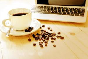 en kopp kaffe, laptop och breda kaffebönor foto