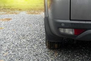 ner av baksidan grå bil parkering på bred grus golv. vit suddig av grönt gräs. miljö av efter regnigt hela området är blött av regn. foto