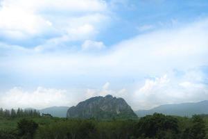 landskapsvy av högt träd framför jordbruksområden. berget har en höga klippa i mitten. under blå himmel och vita clounds. på wang chan, rayong thailand. foto