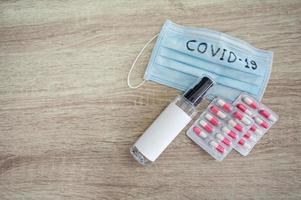 alkoholgelé, medicinsk ansiktsmask med text covid-19 och antibiotika på träbord foto
