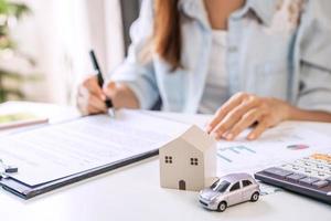 ung kvinna undertecknar ett låneavtal för att köpa ett hus och en bil på fastighetsmäklarkontoret foto