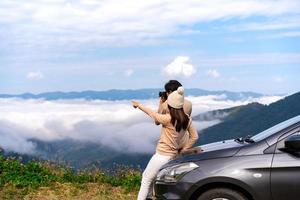 ung kvinna resenärer med bil tittar på ett vackert hav av dimma över berget medan resa kör bilresa på semester foto