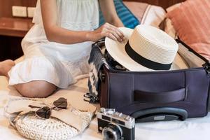 ung asiatisk kvinna som sitter på sängen och packar sin resväska förbereder sig för resor på sommarlovet foto
