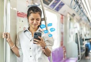 ung asiatisk kvinna passagerare står och använder mobiltelefon inuti tom tunnelbana eller sky train bil, fritid och dagliga liv foto