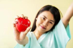 ung kvinna patient visar ett rött hjärta på handen och sittande säng med leenden och ljusa ansiktsuttryck, har bättre symtom på patientavdelningen foto