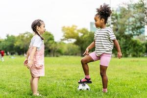 två söta små afroamerikanska spelar fotboll tillsammans på gräset en solig sommardag, motion för hälsan. sport och barn koncept. foto