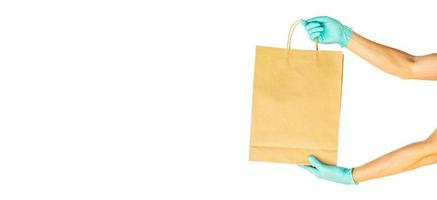 leveransman hand i sterila handskar som håller mat i hantverkspapperspåse isolerad på vit bakgrund med kopia utrymme, säker leverans under en viruskarantän pandemi, stanna hemma. foto