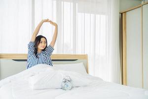 vacker ung kvinna som sträcker sig i sängen med armarna höjda efter uppvaknandet, hälsosam livsstil, wellness-koncept