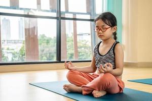 lugn och avslappning, kvinnlig lycka. horisontell, liten asiatisk flicka mediterar medan hon övar yogaklass i skolans gym. frihet koncept. lugn och slappna av, kvinna lycka. tonad bild hälsosamt liv foto