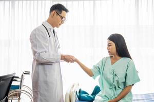 asiatisk man läkare pratar med asiatisk kvinna patient på sjukhuskontoret medan han håller patientens händer gör grundläggande medicinsk undersökning och diagnostik. sjukvård och sjukvård. foto