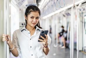 ung asiatisk kvinna passagerare står och använder mobiltelefon inuti tom tunnelbana eller sky train bil, fritid och dagliga liv foto