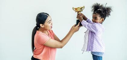 afrikansk amerikansk dotter uttrycker spännande efter att få belöning som trofé från sin mamma, som håller en trofé högt upp foto