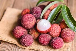 litchifrukt på säck med gröna blad och träbakgrund, färsk mogen litchi skalad från litchiträd vid tropisk frukt Thailand på sommaren foto