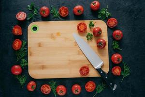 tomatram runt skärbräda av trä. mogna grönsaker och skiva, grön persilja och dill nära köksbräda och kniv. matkonst foto