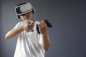Asiatisk man spelar på allvar spel med hjälp av VR-googles och konsoler mot mörkgrå bakgrund. kopieringsutrymme för spelproduktionskoncept. foto