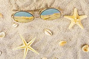 sommar bakgrund. havssand med snäckskal, sjöstjärnor och solglasögon. sommar semester koncept foto