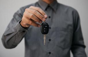 närbild händer som håller bilnycklar. man håller nyckeln till bil ger till agent för försäkring för försäljning. affärsinvestering försäkring bil beslag och bil koncept. foto