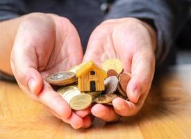 hus- eller hemmodell och mynt till hands med hemnyckel. koncept för lån, fastighetstrappa, finansiellt, bolån, fastighetsinvesteringar, skatter och bonus. foto