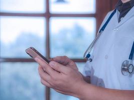 manlig läkare som använder smart telefon hitta information och håller stetoskop på sjukhus. hälso- och medicinkoncept. foto
