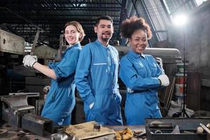 multiracial industriarbetare i säkerhetsuniformer samarbetar med enhet, agerar med verktyg och uttrycker lyckligt arbete tillsammans med leende och glada i mekanisk fabrik, professionell ingenjörsyrke. foto