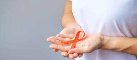 hand som håller orange band för leukemi, njurcancerdagen, världens multipel skleros, crps, självskademedvetenhetsmånad. hälsovård och ordet cancer dag koncept foto