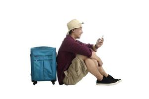 resenär som sitter mot en resväska och använder mobiltelefon