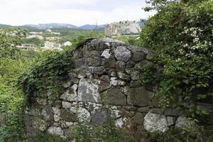 en gammal fallfärdig stenmur av ett tatariskt bostadshus i ett bergsområde med buskar och träd, mot bakgrund av en bergskedja. foto