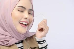 en ung muslimsk kvinna som håller invisalign hängslen i studio, tandvård och ortodontisk koncept.. foto